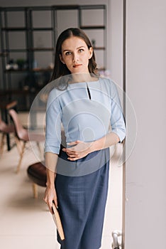 Serious young business woman holding file folder while standing near window in modern office room.