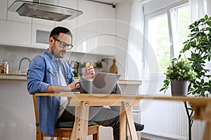 Serious young businessman paying through credit card while shopping online on laptop in home office