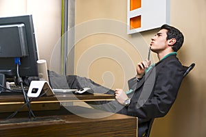 Serious young businessman sitting at desk in office thinking