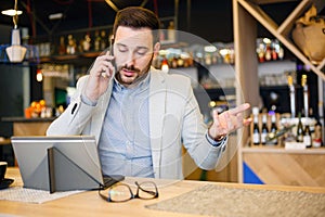 Serious young businessman talking on a phone, working in a cafe