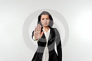 Serious young businesswoman in black formal jacket white shirt showing stop gesture with palm isolated on white background.