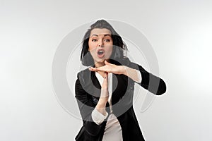 Serious young businesswoman in black formal jacket white shirt showing a timeout gesture, standing over white background. Social