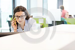 Serious young businesswoman talking on mobile phone in office