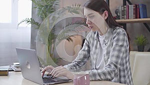 Serious young Caucasian girl typing fast on laptop keyboard. Confident female freelancer working online from home