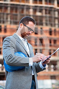 Serious young civil engineer or businessman signing documents on construction site