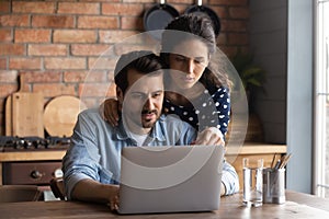 Serious young couple using laptop in cozy kitchen, browsing apps
