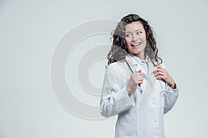 A serious young female Caucasian woman in a laboratory robe, looking at you and holding the phonendoscope out of hand