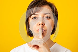 Serious young female holding finger at her lips asking not to make noise or hold tongue and conceal some private confidential