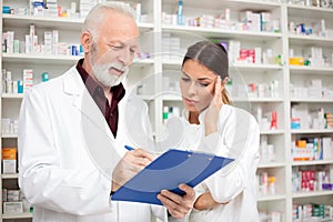 Serious young female and senior male pharmacists standing in front of shelves with medications in a drugstore