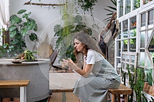 Serious young gardener woman owner holding smartphone reading media news, sitting in home garden