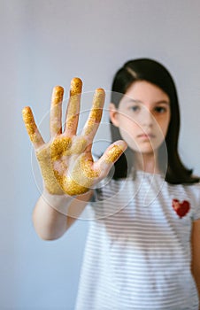 Serious young girl showing her palm hand covered of golden glitter while doing stop sign