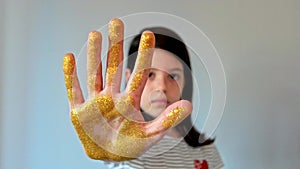 Serious young girl showing her palm hand covered of golden glitter while doing stop sign