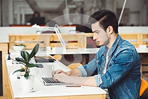 Serious young guy with beard working on laptop