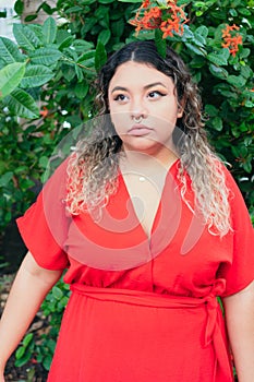 Serious young Hispanic model in red dress outdoors, woman in park