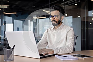 Serious young Indian businessman man working focused on laptop while sitting in office at desk