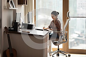Serious Indian female sit at desk holds pen jotting information photo