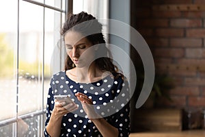 Serious young Latin woman using mobile phone at home