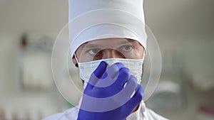 Serious young male doctor putting on Covid-19 face mask in slow motion and looking away. Headshot portrait of Caucasian