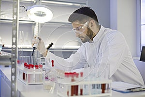 Serious young male scientist using a pipette while working in the pharma laboratory