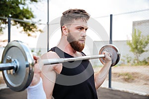 Serious young man athlete standing and holding barbell