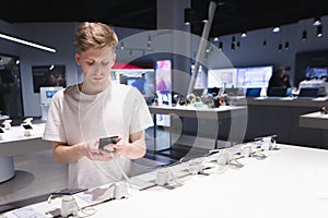 serious young man is buying a smartphone in the electronics store. Buy a smartphone in the tech store