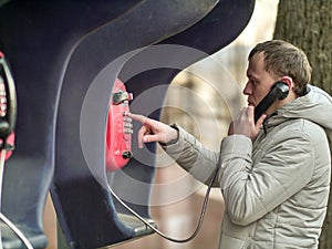 Serious young man calling by red street payphone