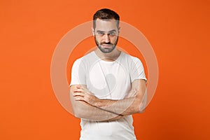 Serious young man in casual white t-shirt posing isolated on bright orange wall background, studio portrait. People