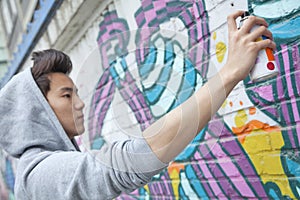 Serious young man concentrating while holding a spray can and spray painting on a wall outdoors