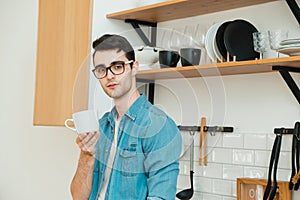 Serious young man drinking tea or coffee in the kitchen, worrying about the situation in the world.