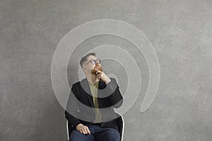 Serious young man in glasses sitting in chair, looking up and thinking about something