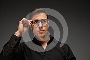 Serious young man, manager in black business classic style shirt putting eyewear on isolated over grey background