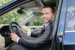 Serious young man of Middle Eastern appearance in a business suit is driving an expensive car