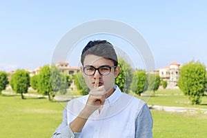 Serious young man placing finger on lips with shhh sign symbol.