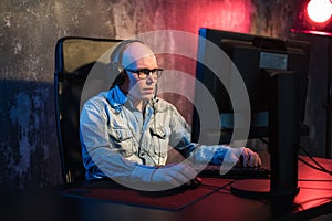 Serious young man sitting and working with computer in dark office