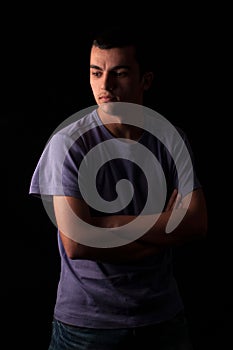 Serious young man standing with arms crossed on black background