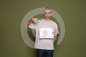 Serious young man student holding white empty paper board on green background