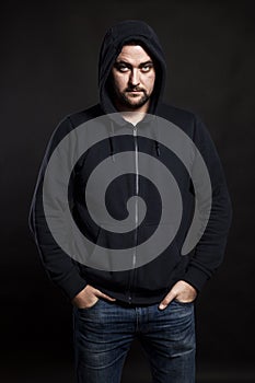 Serious young man in a sweater with a hood on a black background. Banditry and crime. Vertical