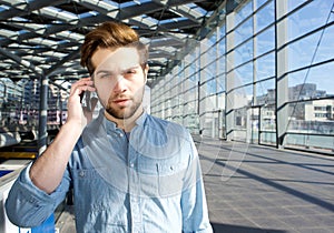 Serious young man talking on mobile phone inside building