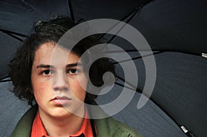 Serious young man under black umbrella