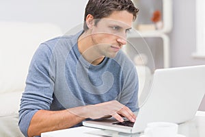 Serious young man using laptop in living room