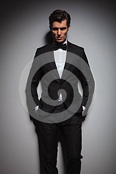 Serious young man wearing tuxedo standing with hands in pockets