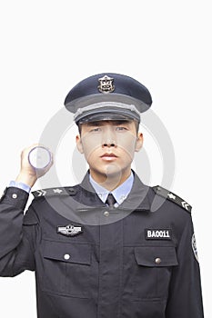 Serious Young Police Officer Shining Flashlight into Camera, Studio Shot