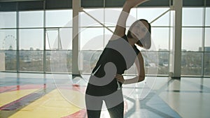 Serious young sports lady in trendy outfit bending sidewards indoors in modern gym
