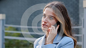 Serious young successful lady business woman girl in blue suit stands on balcony talking mobile phone. Female consultant