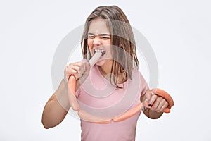 Serious young woman bite one sausage and shrink. She look angry and mad. Isolated on white background.