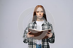 Serious young woman college student holding opened books and looking at camera on gray background.