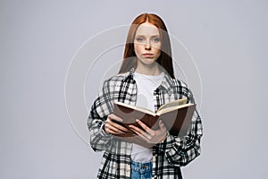 Serious young woman college student holding opened books and looking at camera on gray background.