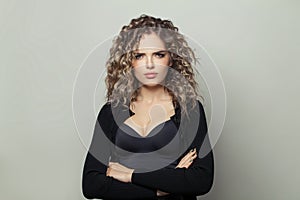 Serious young woman with curly hairstyle standing with crossed arms on white background