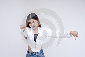 A serious young woman doing a thumbs down gesture while pointing at the camera. Isolated on a white background