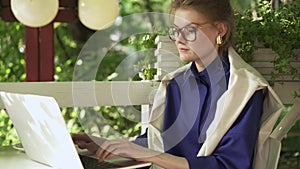 Serious young woman in glasses working with laptop in a summer cafe